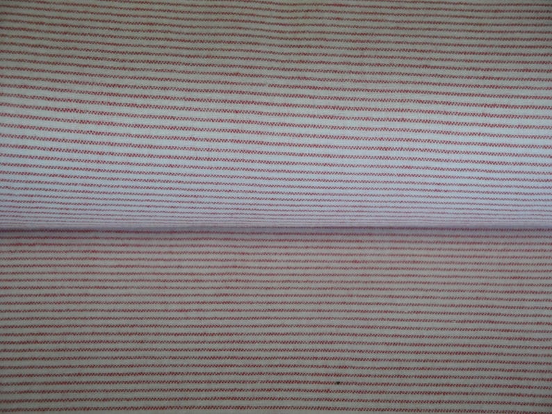 May include: Close-up of a fabric with a repeating pattern of thin, horizontal red stripes on a white background. The fabric is folded, showing the pattern on both the top and bottom layers. The stripes are evenly spaced.