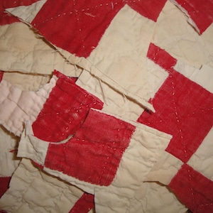 May include: Close-up of a vintage quilt with a red and cream checkerboard pattern. The quilt squares are stitched together, showing signs of wear and age. The fabric has a slightly faded appearance.