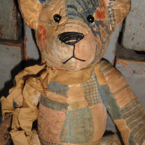 Puede incluir: Un oso de peluche de patchwork hecho de varios retazos de tela en tonos apagados de azul, bronceado y patrones florales descoloridos. El oso presenta ojos de bot&oacute;n negros, una nariz y boca cosidas a mano con hilo negro y una bufanda de tela.