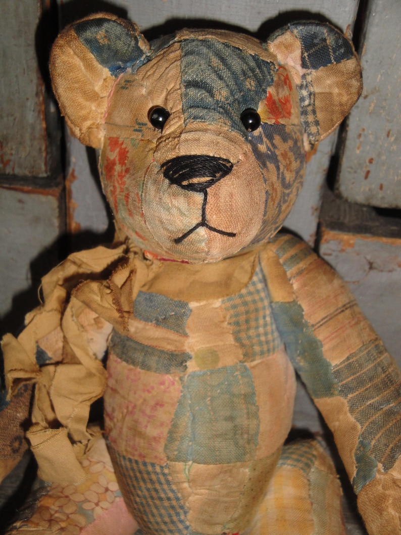 Puede incluir: Un oso de peluche de patchwork hecho de varios retazos de tela en tonos apagados de azul, bronceado y patrones florales descoloridos. El oso presenta ojos de bot&oacute;n negros, una nariz y boca cosidas a mano con hilo negro y una bufanda de tela.
