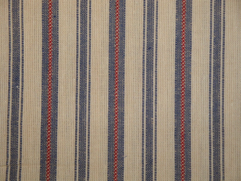May include: Close-up of a woven fabric with a cream background and vertical stripes. The stripes alternate between navy blue and red, creating a classic, textured pattern. The fabric appears to be a natural fibre.