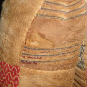 May include: A close-up of a vintage quilt with a patchwork design. The quilt is made of different fabrics in shades of red, white, and blue. The fabric is worn and faded, showing signs of age. The quilt has a hole in the center, revealing the fabric underneath.