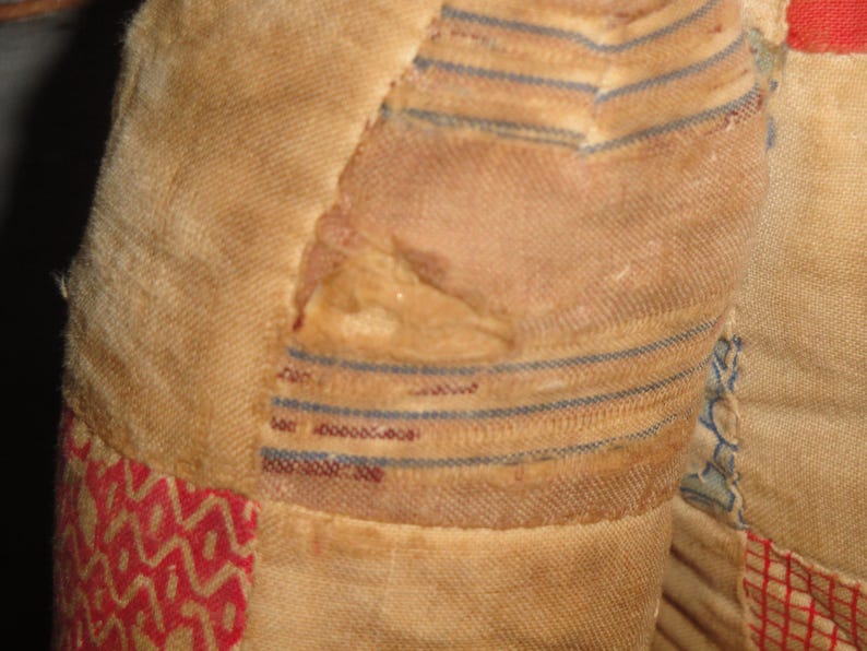 May include: A close-up of a vintage quilt with a patchwork design. The quilt is made of different fabrics in shades of red, white, and blue. The fabric is worn and faded, showing signs of age. The quilt has a hole in the center, revealing the fabric underneath.