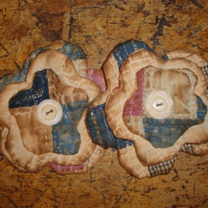 May include: Two fabric flowers with a blue, red, and white patchwork design. Each flower has a white button in the center.