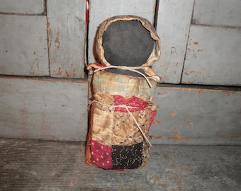 May include: A vintage rag doll with a black fabric head and a patchwork quilt body. The doll is made of fabric scraps in shades of red, brown, gold, and black.