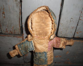 May include: A vintage rag doll with a quilted patchwork dress. The doll has a brown fabric head with a stitched-on face and a blue and pink quilted hood.