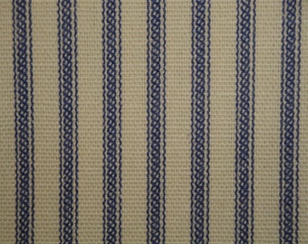 May include: A close-up of a beige fabric with blue stripes. The fabric has a woven texture and the stripes are made of a darker blue thread.