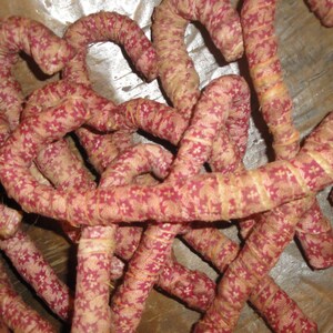 K&ouml;nnte beinhalten: Eine Ansammlung von gebogenen, stoffbezogenen St&auml;ben mit einem sich wiederholenden Muster aus kleinen roten Blumenformen auf beigem Grund. Jeder Stab ist mit einem durchgehenden Streifen aus bedrucktem Textil umwickelt, was eine texturierte, zylindrische Optik erzeugt.