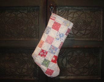May include: A patchwork Christmas stocking with red, white and blue squares. The stocking is hanging on a dark wooden door with a decorative pattern.
