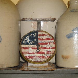 May include: A vintage scale with a red, white, and blue American flag design. The scale reads "I pledge allegiance to the flag of the United States of America".