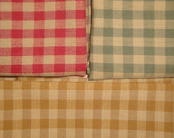May include: Close-up of three fabric swatches with a classic gingham pattern. The colors include red and white, sage green and white, and golden yellow and white. The fabric has a woven texture.