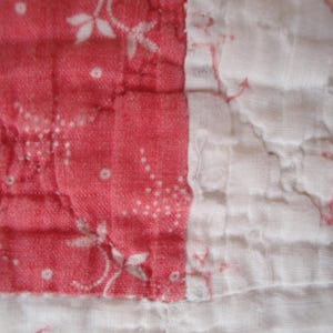 Op de afbeelding: Een gewatteerd textiel met afwisselende panelen in koraalroze en wit. De koraalroze secties tonen een delicaat wit bloemen- en stippenpatroon, terwijl de witte secties een subtiele, vage koraalroze bloemenprint bevatten.