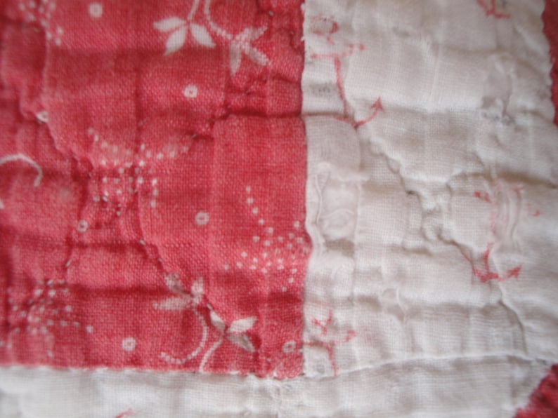 Op de afbeelding: Een gewatteerd textiel met afwisselende panelen in koraalroze en wit. De koraalroze secties tonen een delicaat wit bloemen- en stippenpatroon, terwijl de witte secties een subtiele, vage koraalroze bloemenprint bevatten.