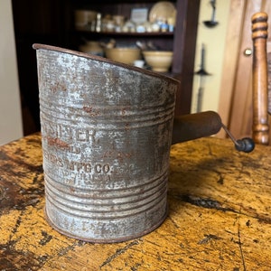 May include: A vintage metal scoop with a wooden handle. The scoop is rusty and has the words "Whisper Flour Mills Mfg Co." printed on the side.