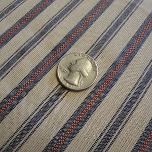 May include: A silver coin lies on striped fabric. The fabric features diagonal stripes in beige, blue, and red. The coin displays a profile and the year 1966. The fabric's stripes are approximately 1.5 cm wide.