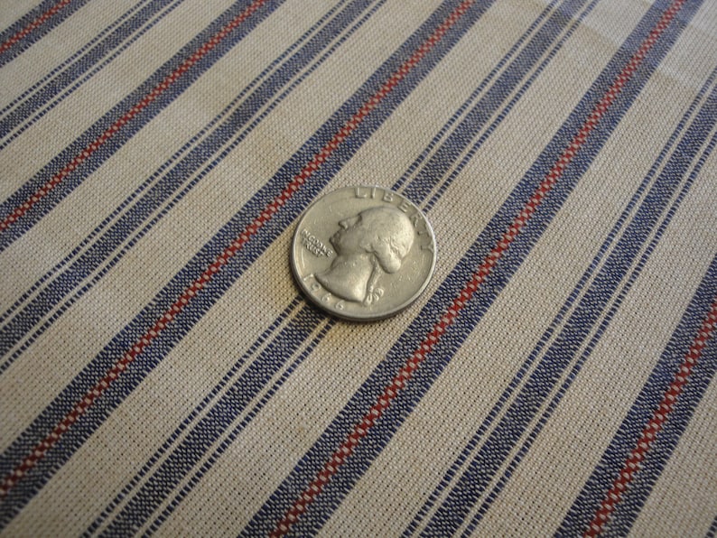 May include: A silver coin lies on striped fabric. The fabric features diagonal stripes in beige, blue, and red. The coin displays a profile and the year 1966. The fabric's stripes are approximately 1.5 cm wide.