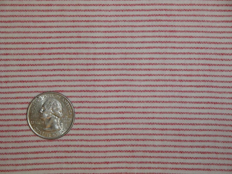 May include: Close-up of a fabric with a repeating pattern of thin, horizontal red stripes on a cream background. A U.S. quarter coin is in the lower left corner for scale. The fabric appears to be cotton or a similar woven material.