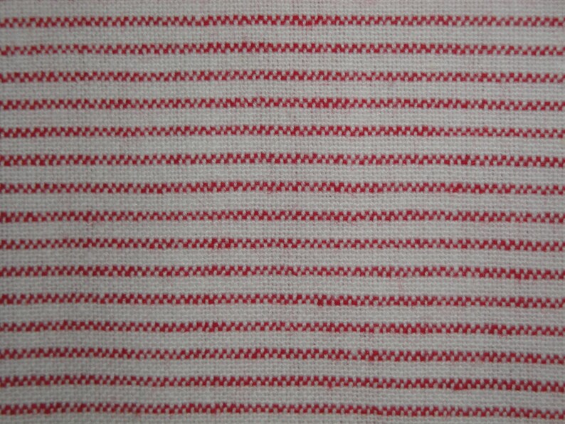 May include: Close-up of a woven fabric with a repeating pattern of horizontal red stripes on a white background. The red stripes have a textured, zig-zag appearance, creating a visually interesting design. The fabric appears to be a natural fiber.