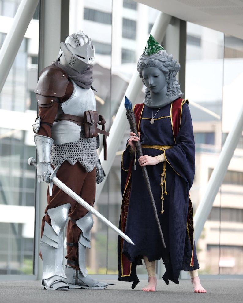 Puede incluir: Dos cosplayers con atuendos de fantas&iacute;a. Uno lleva una armadura plateada, un casco y una espada. El otro viste una t&uacute;nica azul oscuro con una pieza para la cabeza similar a una estatua y sostiene un bast&oacute;n con un cristal azul.
