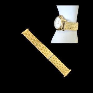 May include: A gold-tone watch with a round white face and a textured brick-link metal strap. The watch features a gold bezel and matching gold-tone hands. A separate, matching gold-tone metal watch strap is displayed alongside the watch.
