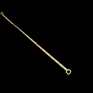 May include: A long, thin, gold-coloured chain featuring a series of repeating, elongated, diamond-shaped links connected by small, straight bars. The chain terminates at one end with a small, rounded, D-shaped metal loop or clasp component.