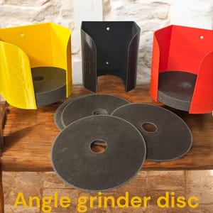 Może przedstawiać: Trzy 3D-wydrukowane uchwyty na tarcze do szlifierki kątowej w kolorze żółtym, czarnym i czerwonym. Uchwyty są zamontowane na drewnianej powierzchni, przed którymi znajduje się stos tarcz ściernych. Tekst "Angle grinder disc holder" jest napisany na żółto na dole obrazu.