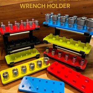 Puede incluir: Una colección de soportes para llaves de colores rojo, amarillo, azul y negro. Los soportes están diseñados para organizar llaves de vaso y llaves. El texto "TABLE AND WALL SOCKET WRENCH HOLDER" se muestra en la parte superior de la imagen.