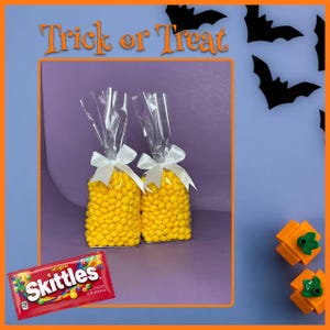 May include: Two cellophane bags filled with yellow candies, tied with white bows, and a red Skittles candy package. The image has a Halloween theme with the words "Trick or Treat" and bat silhouettes.