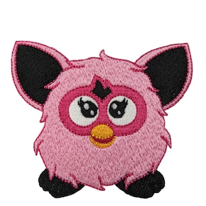 May include: Embroidered patch featuring a pink creature with large, white-rimmed eyes, a yellow beak, and black ears and feet. The patch has a fluffy texture and is likely designed for application on clothing or accessories.
