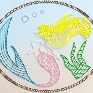 May include: An embroidered design featuring a mermaid within an oval frame. The mermaid has yellow hair, a pink tail, and white skin. Blue seaweed and green plants are also included. The design is framed by a brown rope-like border, with bubbles in the background.
