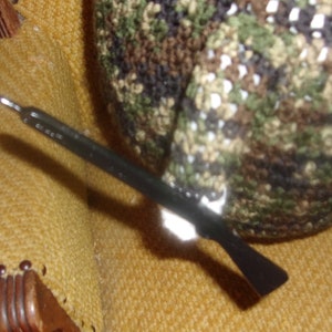 Puede incluir: Un ganchillo negro y plateado con un gorro de crochet de camuflaje en el fondo.