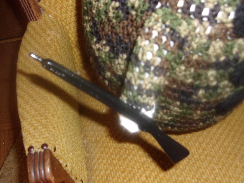 Puede incluir: Un ganchillo negro y plateado con un gorro de crochet de camuflaje en el fondo.