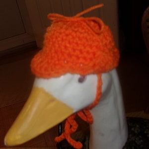 Puede incluir: Un ganso blanco con un gorro de punto naranja con una larga correa de punto naranja.