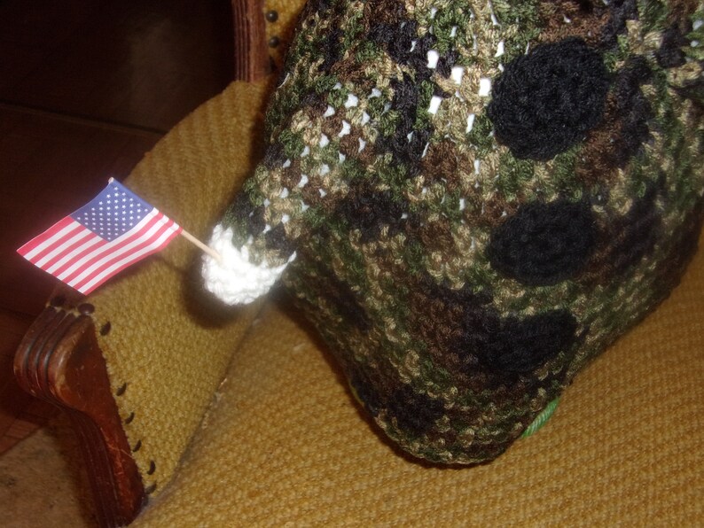 Puede incluir: Una peque&ntilde;a bandera estadounidense est&aacute; unida a un palo de madera y colocada en una silla de tela marr&oacute;n y beige. La bandera es roja, blanca y azul. La silla est&aacute; cubierta de una tela marr&oacute;n y beige con un patr&oacute;n tejido.