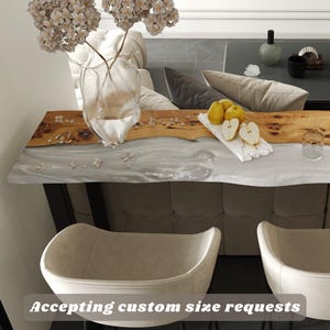 May include: A contemporary interior scene with a live edge wooden table and a marble-effect surface. A clear glass vase holds beige flowers, and a plate of pears sits on the table. Two beige chairs with black legs are in the foreground. Text: Accepting custom size requests.