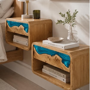 May include: Two floating nightstands made of light-toned wood with a live edge design featuring a vibrant blue resin inlay. Each unit has an open storage shelf containing books titled Kinfolk, Live Beautiful, and This Is Home.