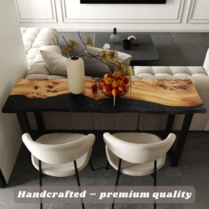 May include: A rectangular console table featuring a natural live-edge wood slab with prominent grain patterns joined to a solid black resin section. The table is supported by black metal legs and includes the text Handcrafted – premium quality.