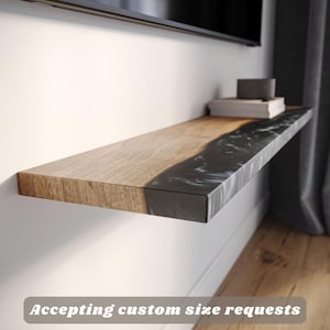 May include: A floating wooden shelf with a live edge design, featuring a dark, marbled resin inlay. The shelf is mounted on a white wall, with books and a small speaker on top. Text on the image reads: "Accepting custom size requests."