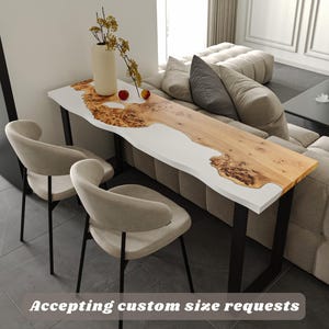 May include: A live edge console table with a white epoxy resin river and natural wood grain. The table has black metal legs and is paired with two beige chairs. The text "Accepting custom size requests" is visible.