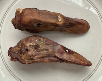 May include: Two dried duck heads on a white ceramic plate with the letters "U", "B", and "T" on the rim.