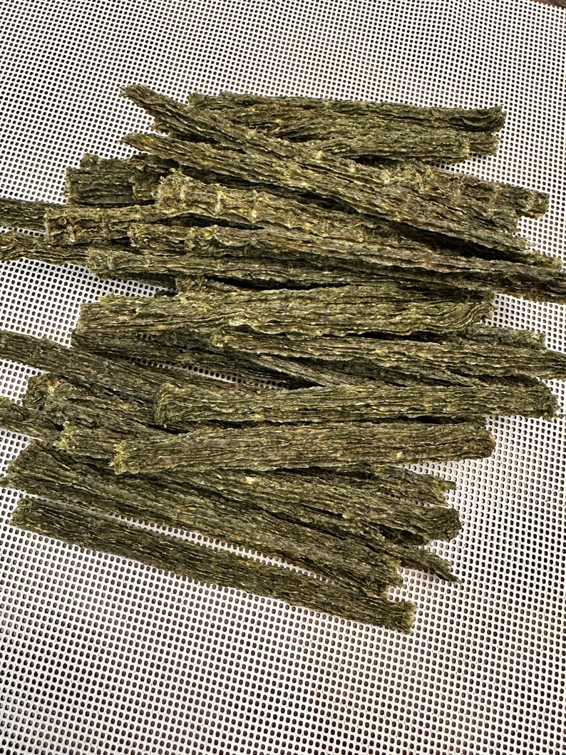 K&ouml;nnte beinhalten: Ein Stapel getrockneter Algensnacks, die auf einer wei&szlig;en Netzfl&auml;che angeordnet sind. Die Snacks sind lang und d&uuml;nn und haben eine dunkelgr&uuml;ne Farbe.