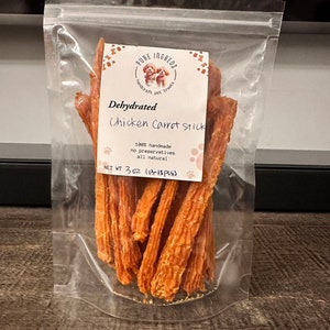K&ouml;nnte beinhalten: Ein transparenter Plastikbeutel gef&uuml;llt mit dehydrierten H&uuml;hner- und Karotten-Hunde-Leckerlis. Das Etikett lautet "PURE INGRED", "handcraft pet treats", "Dehydrated Chicken Carrot Stick", "100% handmade", "no preservatives", "all natural", und "NET WT 3 OZ (13-15 PCS)".