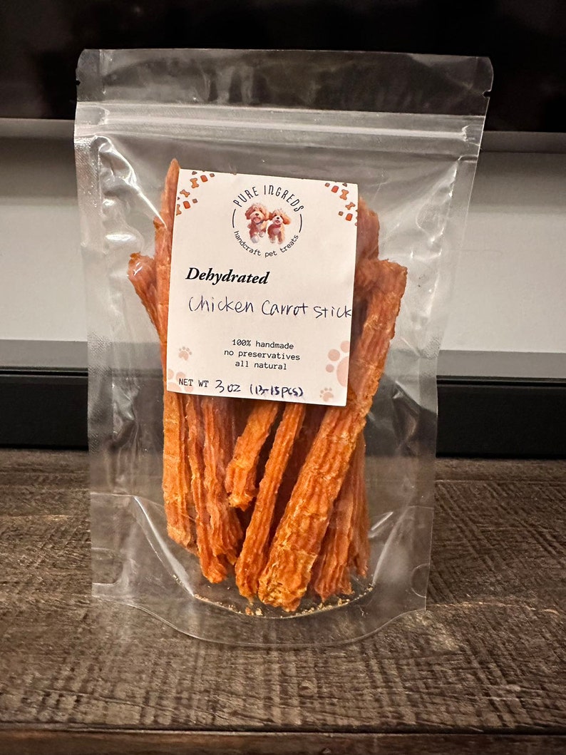K&ouml;nnte beinhalten: Ein transparenter Plastikbeutel gef&uuml;llt mit dehydrierten H&uuml;hner- und Karotten-Hunde-Leckerlis. Das Etikett lautet "PURE INGRED", "handcraft pet treats", "Dehydrated Chicken Carrot Stick", "100% handmade", "no preservatives", "all natural", und "NET WT 3 OZ (13-15 PCS)".