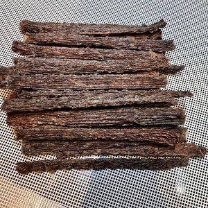 K&ouml;nnte beinhalten: Nahaufnahme eines Stapels d&uuml;nner, dunkelbrauner Rindfleisch-Jerky-Streifen auf einer wei&szlig;en Netzfl&auml;che.