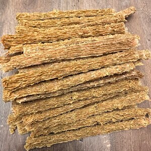 K&ouml;nnte beinhalten: Ein Stapel d&uuml;nner, brauner Hunde-Kauartikel. Die Leckerlis sind lang und schmal und haben eine leicht strukturierte Oberfl&auml;che.
