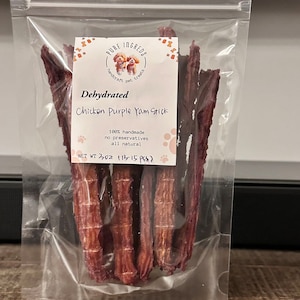 K&ouml;nnte beinhalten: Ein transparenter Plastikbeutel mit dehydrierten H&uuml;hner- und lila S&uuml;&szlig;kartoffel-Hunde-Leckerlis. Der Beutel hat ein Etikett mit der Aufschrift "PURE INGREDS handcraft pet treats Dehydrated Chicken Purple Yam Stick 100% handmade no preservatives all natural NET WT 3 OZ (113-15 PCS)"