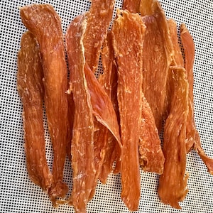 May include: A pile of thin, dried, brown chicken strips on a white, textured surface.