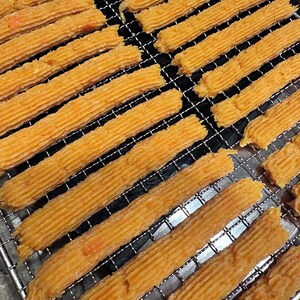 K&ouml;nnte beinhalten: Nahaufnahme eines Drahtgestells mit langen, d&uuml;nnen, orangefarbenen Streifen aus Essen. Die Streifen sind in Reihen angeordnet und leicht gekr&uuml;mmt.