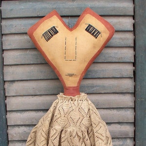 May include: A handmade heart-shaped doll with a brown crocheted dress and a red heart in her hands. The doll has a heart-shaped head with a stitched-on face and black eyelashes.