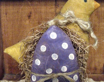 May include: A purple egg with white polka dots is nestled in straw and surrounded by a yellow chick with a brown twine bow.
